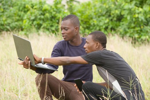 two young men working on laptop outdoors