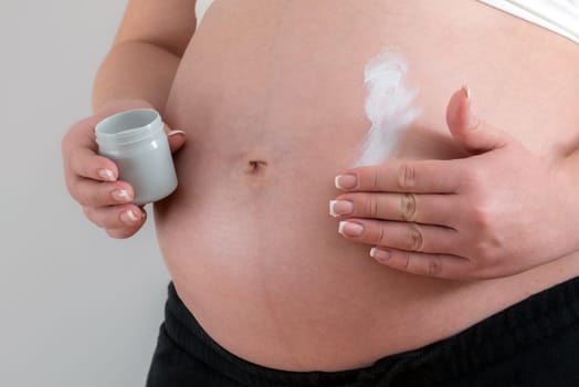 Pregnant woman applying cream on her belly for healing and skin elasticity