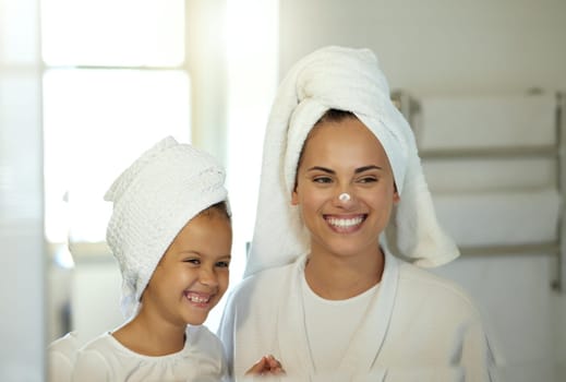 Playful mother and daughter doing a hygiene, skincare routine together in the bathroom. Mom teaching her adorable child a grooming and beauty treatment regime. Parent and little girl applying lotion