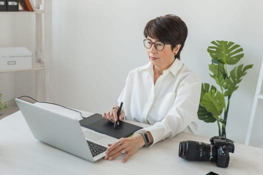 Mature intelligent woman working with computer and graphic tablet and stylus. She is a successful self employed retoucher and photograph