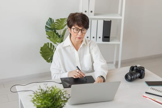 Mature intelligent woman working with computer and graphic tablet and stylus. She is a successful self employed retoucher and photograph