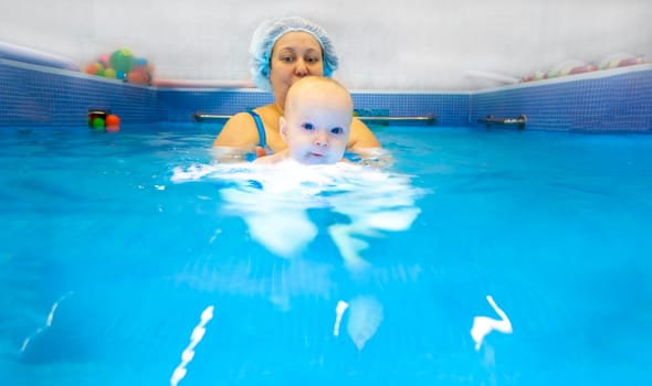 Adorable baby girl enjoying swimming in a pool with her mother early development class for infants teaching children to swim and dive.