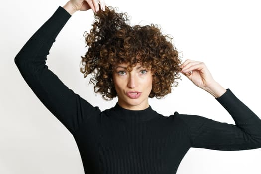 Young woman touching curly hair against white wall