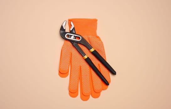 Orange glove and metal universal adjustable wrench on a beige background, top view