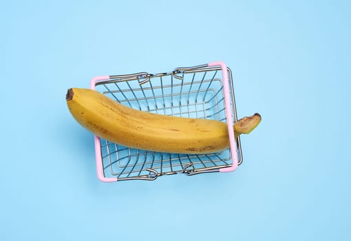 A ripe banana in a miniature shopping cart on a blue background, representing the concept of selling fruits and vegetables