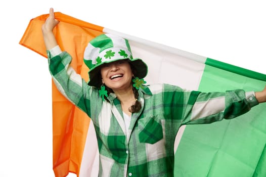 Pretty woman in St Patrick's hat and clover leaves earrings, smiling, carrying flag of Ireland. Irish culture traditions