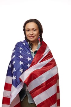 Proud multiethnic woman wrapped in United States of America flag, looking at camera on isolated white background