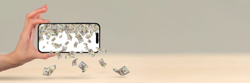 Money is falling from a mobile phone, a hand is holding a phone, US dollars are pouring out of the phone. Financial investment concept from mobile app.