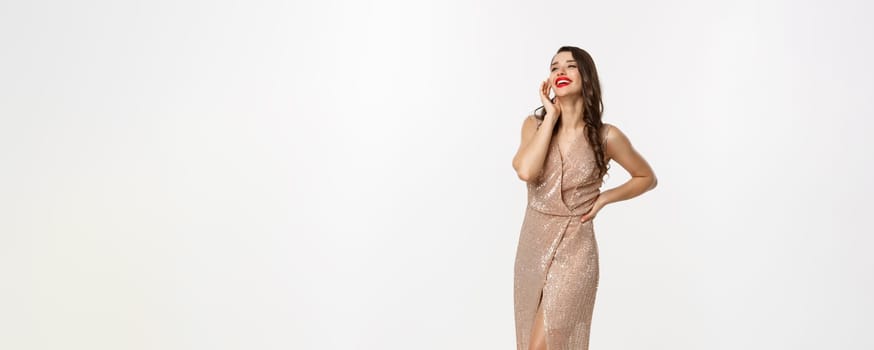 Party and celebration concept. Full-length of perfect woman in elegant dress laughing, standing near Christmas presents, white background.