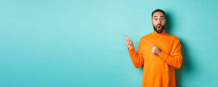 Impressed young man with beard, reacting to promo banner, pointing fingers left, showing logo and looking surprised, standing over turquoise background