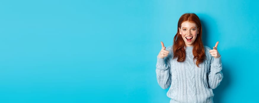 Cheerful teenage girl showing approval, make thumbs up and agree, liking something, standing over blue background