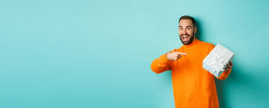Holidays and celebration concept. Excited man receiving gift, looking happy at present and smiling, standing over blue background