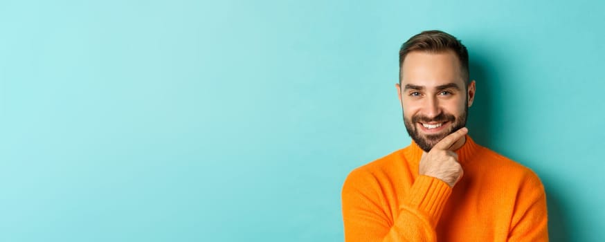 Close-up of handsome and confident man with beard smiling, looking thoughtful at camera, have plan, standing over light blue background