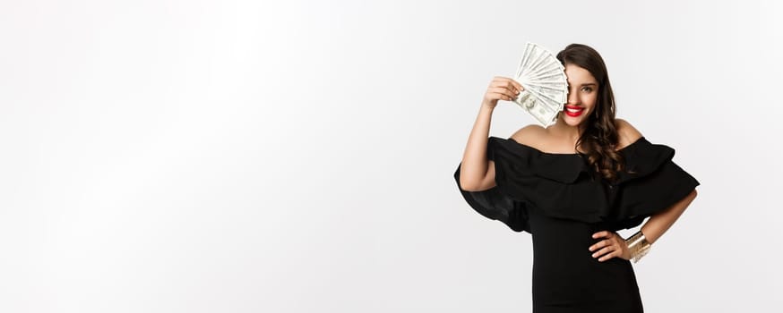 Beauty and shopping concept. Fashionable woman with red lips, showing dollars and smiling, standing over white background with money