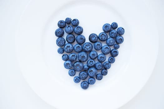 ripe blueberries in a heart shape on a white plate