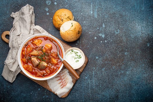 Ukrainian Borscht, red beetroot soup with meat, in white bowl with sour cream, garlic buns Pampushka and salo slices, rustic stone background. Traditional authentic dish of Ukraine, space for text