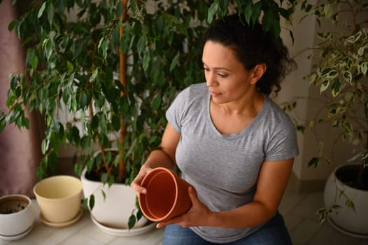 Beautiful multi-ethnic woman, amateur gardener floriculturist holding a clay pot, enjoying floricultural hobby indoor