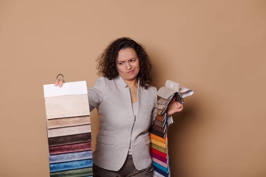 Doubtful woman pointing at fabric samples, having some difficulties on choosing upholstery materials in furniture store