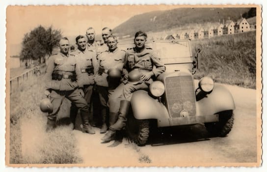 Vintage photo shows German Nazi soldiers stand at convertible.