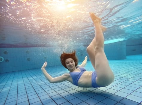 Teen girl swimming under water in blue pool