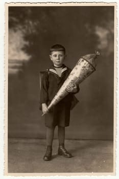 Vintage photo shows pupil boy with school cone. Studio photo with sepia tint.