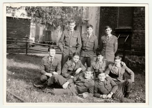 Vintage photo shows soldiers pose in front of barracks. Black white antique photo.