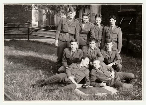 Vintage photo shows soldiers pose in front of barracks. Black & white antique photo.