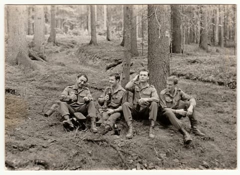 Vintage photo shows soldiers pose with beer bottles outdoors. Black & white antique photo.