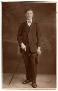 Vintage photo shows a young man holds walking stick. Black white photography with sepia effect.