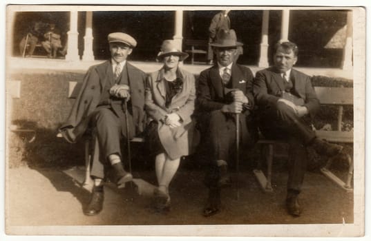 Vintage photo shows men and woman sit on a bench in spa resort. Black white antique photography.