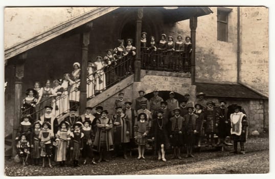 Vintage photo shows a big group of people actors and actresses in historic costumes. They stands in the castle courtyard.