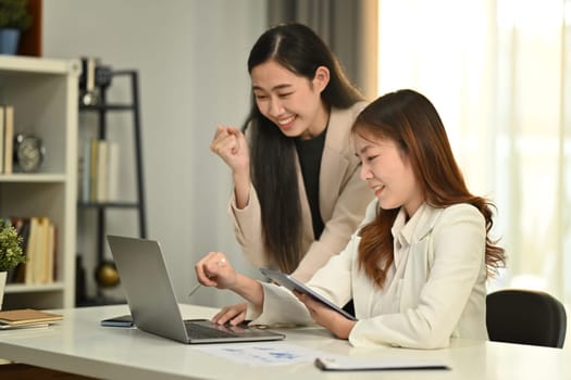 Young asian female employees analyzing financial data, using laptop computer at meeting table
