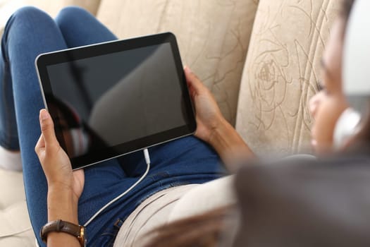 Woman in headphones holds tablet and lies on sofa
