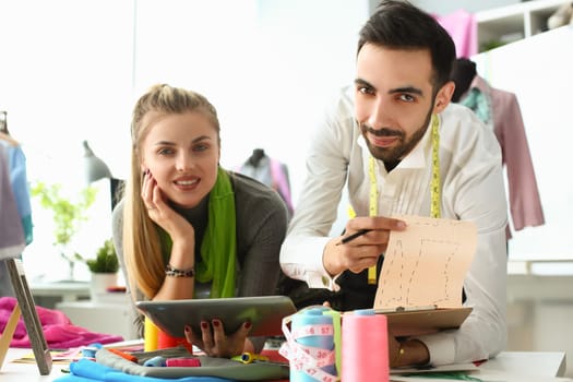 Young business woman stylist seamstress holding tablet male colleague showing sketches of clothes