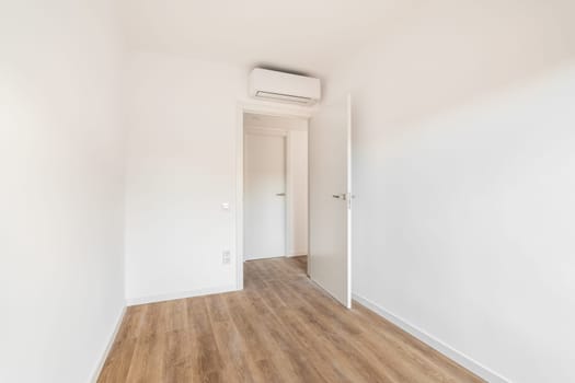 View of the front door to a small white air-conditioned room with wooden floor in a hotel. Concept of simple renovation or an empty apartment after move