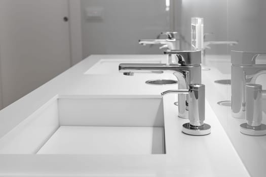 Close-up of white sink with large and small taps for filtering drinking running water. Concept of clean drinking water and high-tech purification system