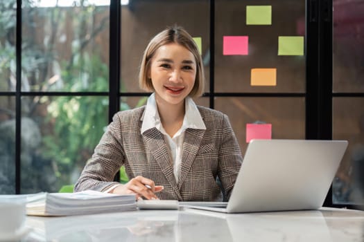Portrait of smiling beautiful business asian woman with working in office desk using laptop