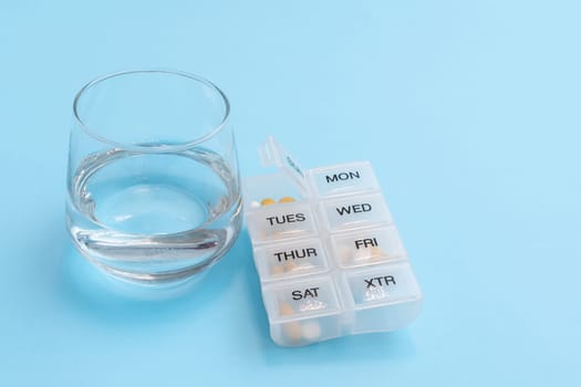 Organizer for taking pills by day of the week and a glass of water as a concept of daily health