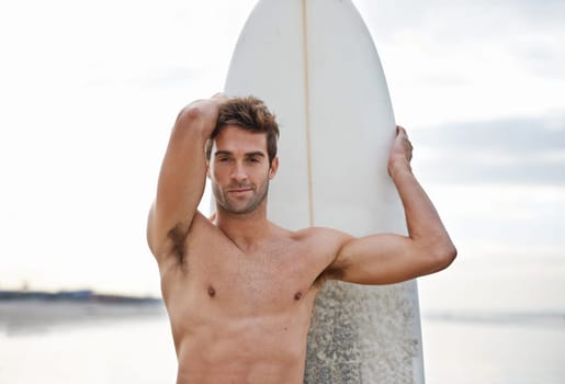 Surfing gets him fit. a bare-chested male surfer with his surfboard at the beach.