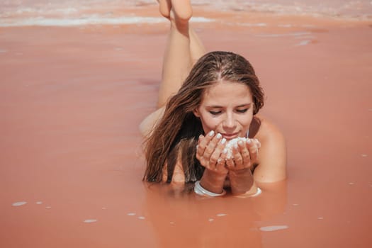 Young woman with long hair in pink salty lake with crystals of salt. Extremely salty pink lake, colored by microalgae with crystalline salt depositions. Spa, beauty and health care concept.