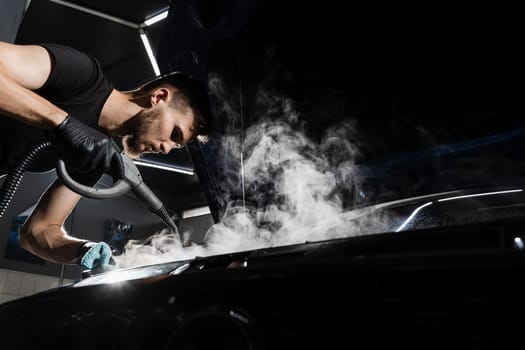 Process of steam cleaning car engine from dust and dirt. Steaming washing of motor of auto in detailing auto service.