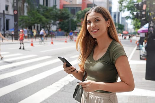 Brazilian woman using smartphone looking away on Paulista Avenue, Sao Paulo, Brazil