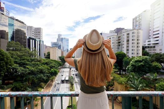 Tourism in Sao Paulo. Back view of beautiful traveler girl holding hat enjoying view of Sao Paulo cityscape, Brazil.