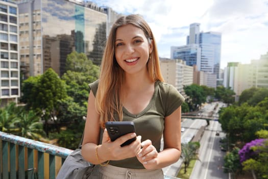 Portrait of young Brazilian woman holding mobile phone looks at camera, Sao Paulo, Brazil