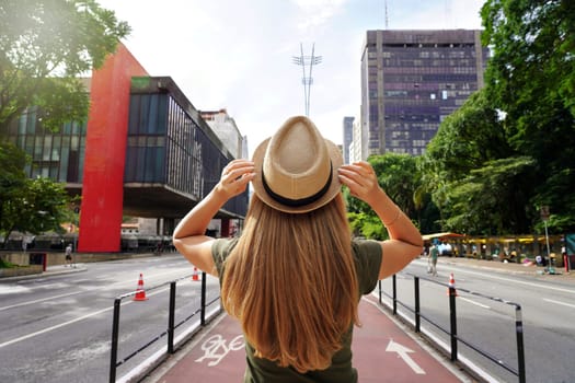 Tourism in Sao Paulo. Back view of beautiful traveler girl with hat walking on the Paulista Avenue, Sao Paulo, Brazil.