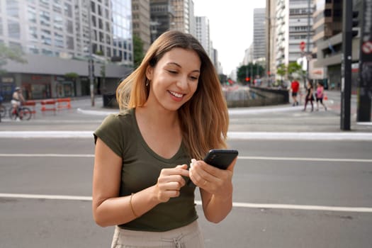 Smiling girl using smartphone on Paulista Avenue, Sao Paulo, Brazil
