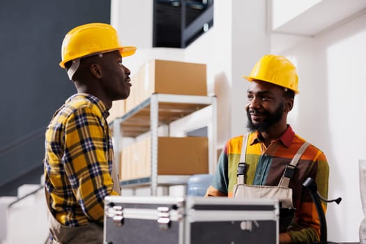 Two african american warehouse colleagues chatting at counter desk