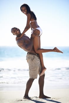 Lifted by their love. A african-american woman being lifted into the air by her strong boyfriend on the beach.