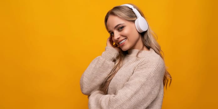young woman with blond hair and with white headphones listens to music on an orange background