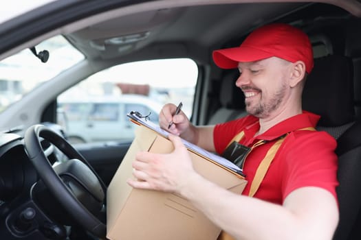 Happy delivery man with cardboard box checklist in van